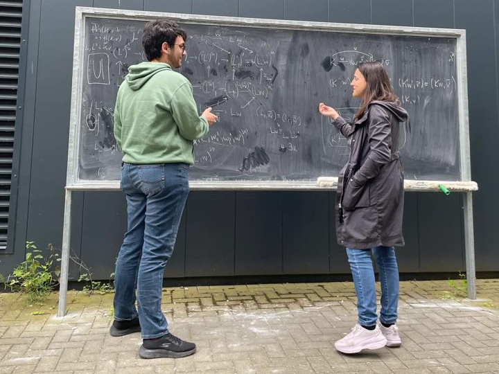 Simone and Anna discussing mathematics in front of a blackboard.